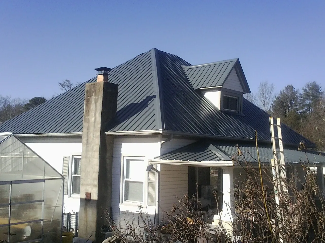 Dark blue standing seam metal roof on a white farmhouse with dormer — Slate & Tile Roof Repair by Roofing Brothers in Trout Creek