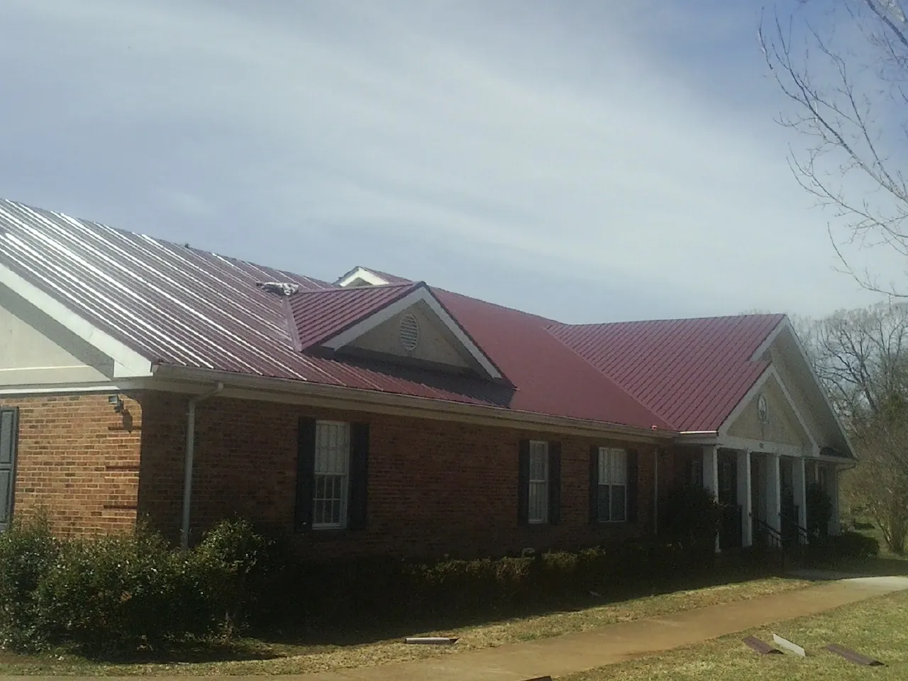 Red metal roof with gabled entries on a long brick building, from a Hail Damage Roof Repair job in Trout Creek
