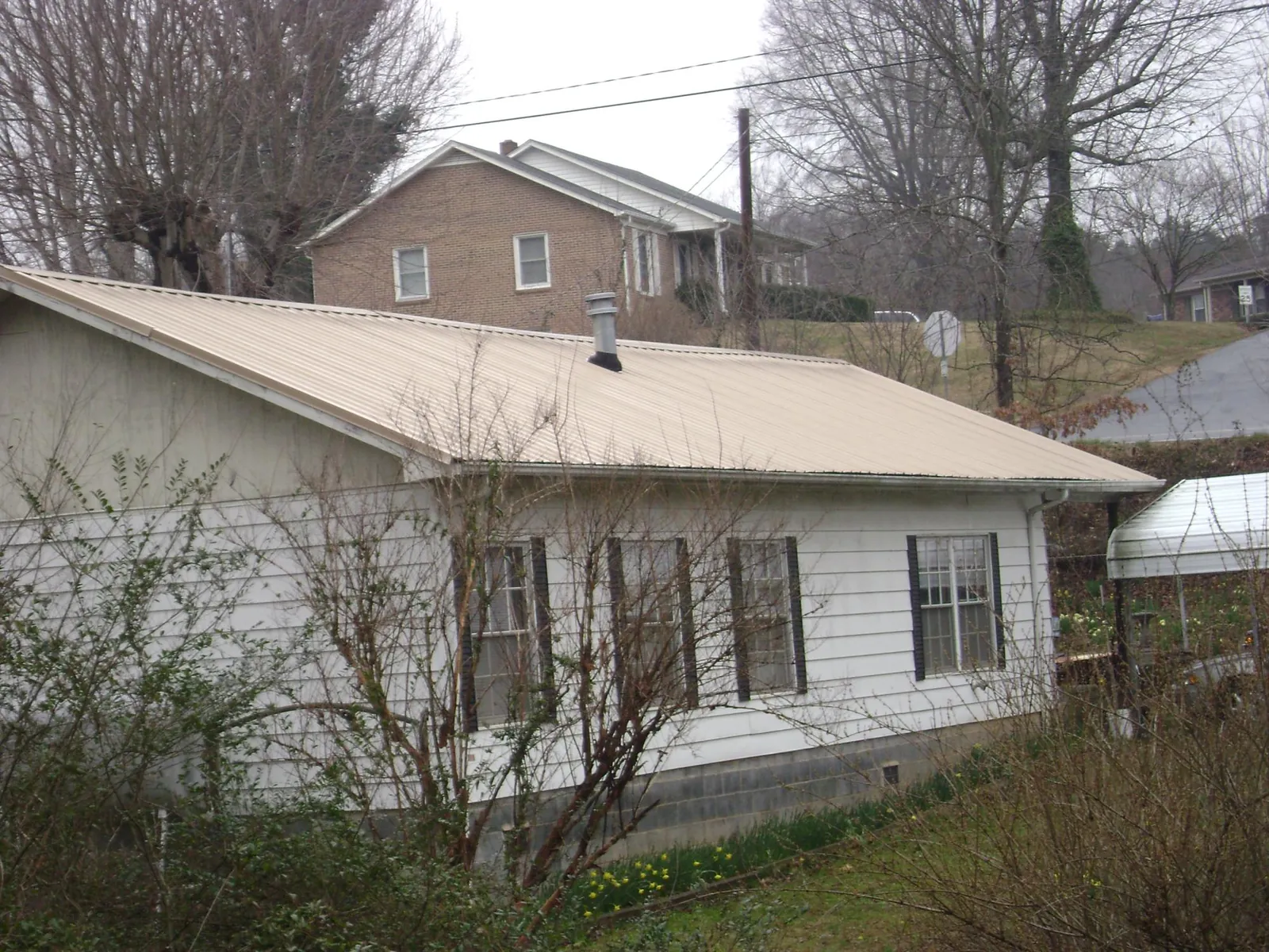 Tan metal roof on a white sided house set into a hillside — Commercial Roofing by Roofing Brothers in Trout Creek