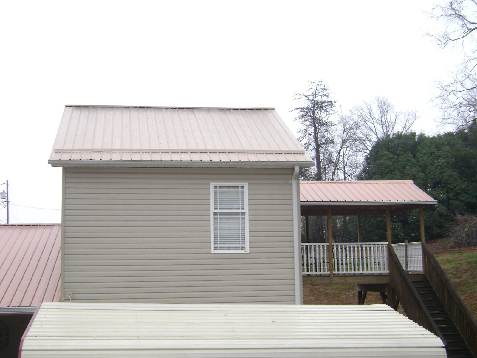 Tan metal roofs on a two story addition and attached porch, from a Roof Replacement job in Trout Creek
